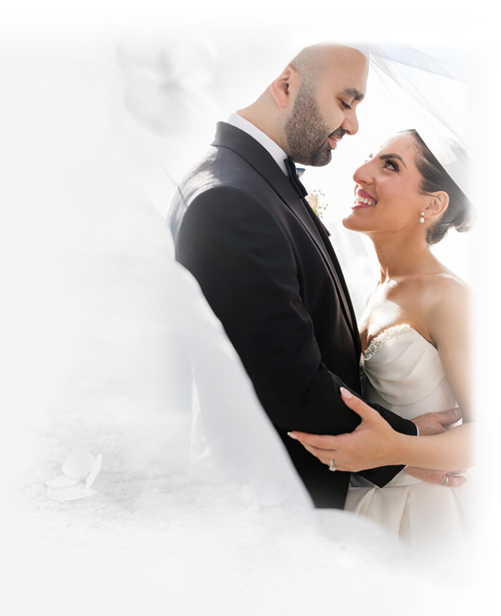 Bride and groom embracing and smiling at each other beneath a sheer wedding veil.